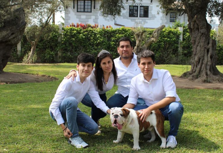 A family posing with a bulldog in a sunny garden setting.