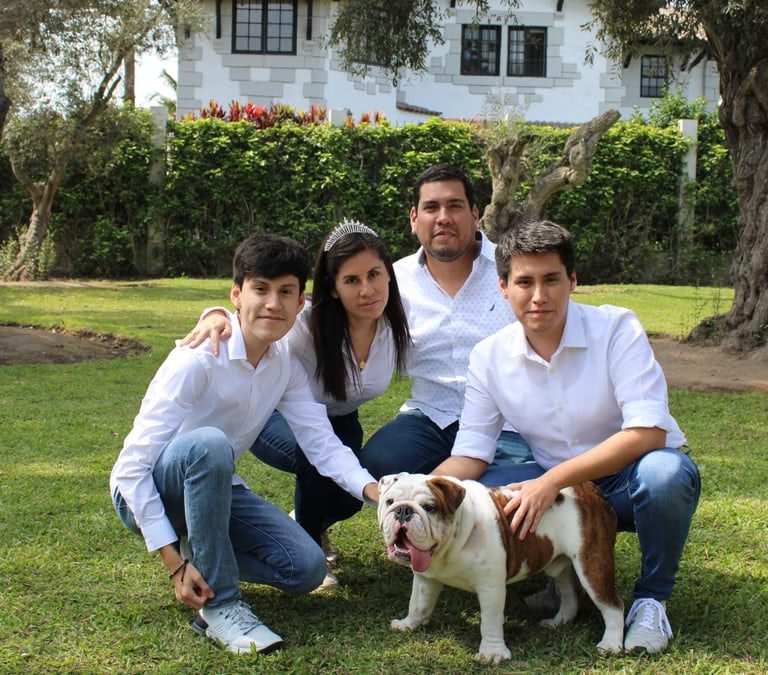 A family posing with a bulldog in a sunny garden setting.
